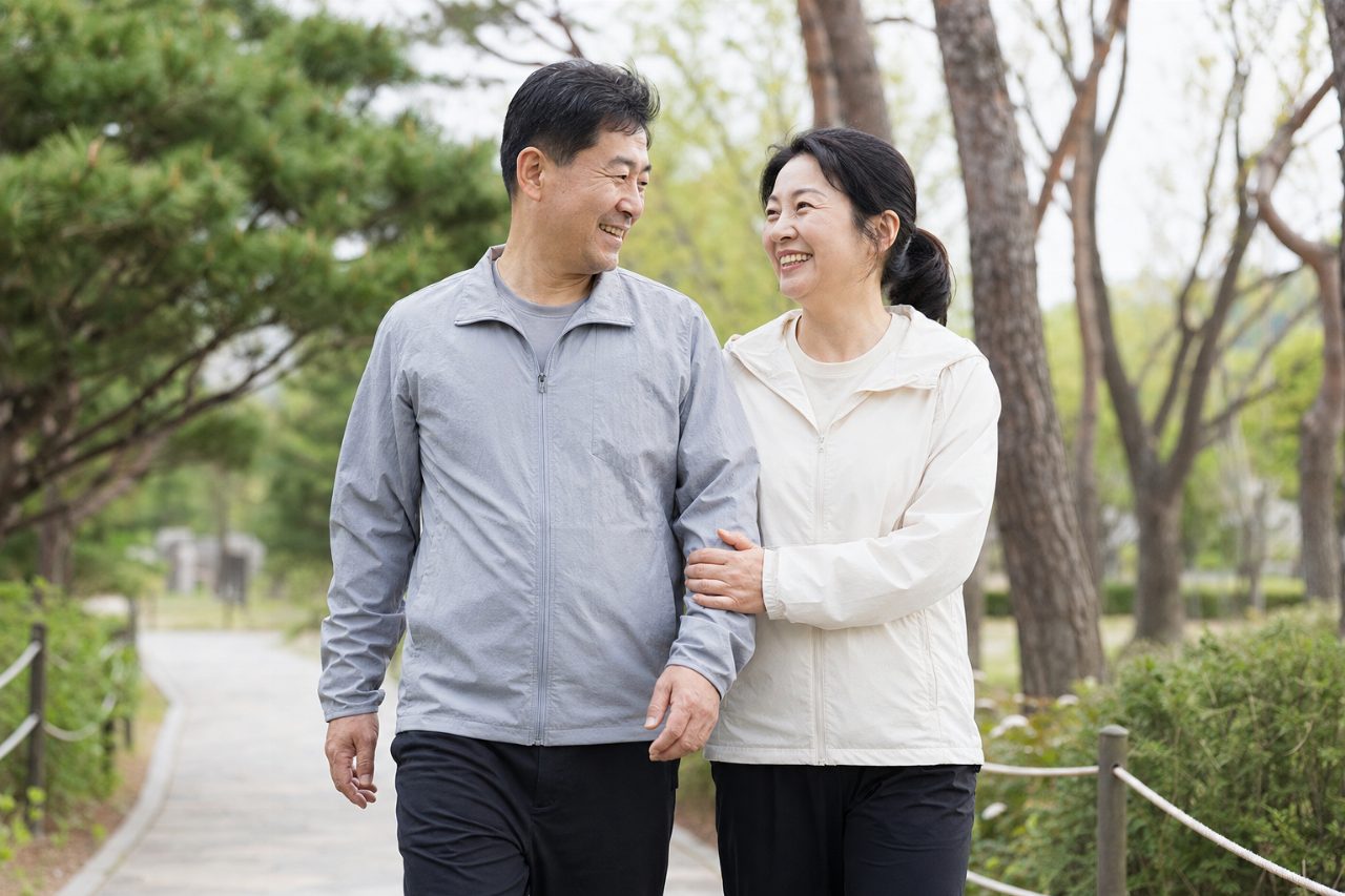 공원에서 가볍게 걷는 중년 남성과 여성이 활짝 웃고 있다.